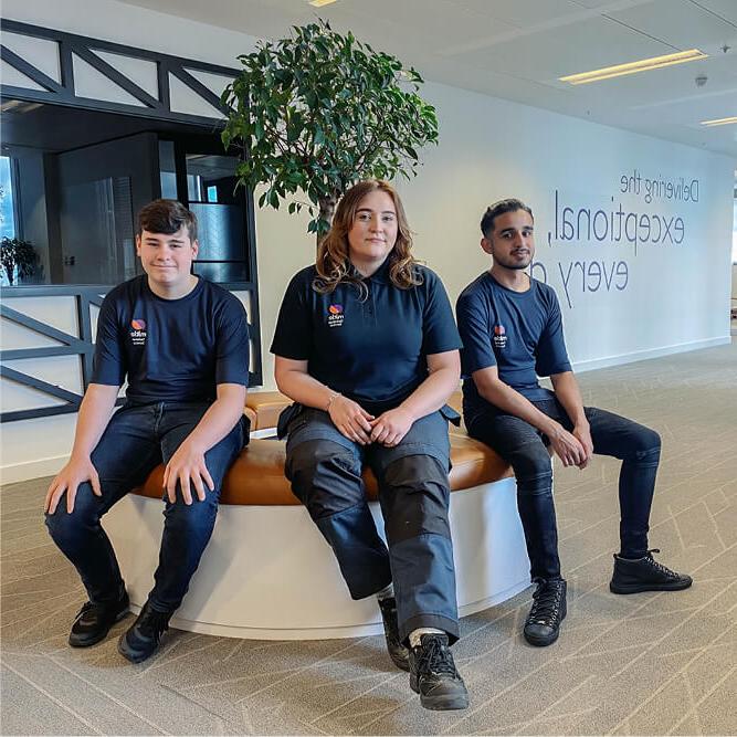 Three apprentices in Mitie t-shirts sitting in an office environment