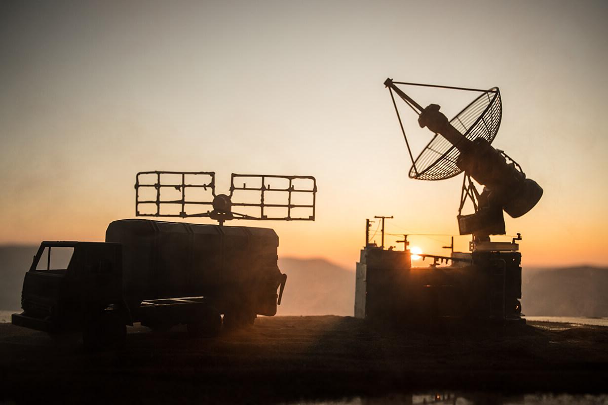 Silhouette of mobile air defence truck with radar antenna during sunset. Satellite dishes or radio antennas against evening sky.